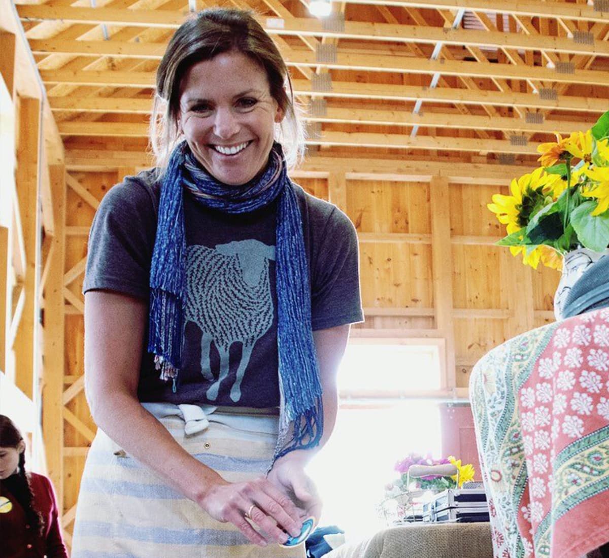 A woman with a blue t-shirt and scarf cutting pieces of cheese in a wooden barn-like structure