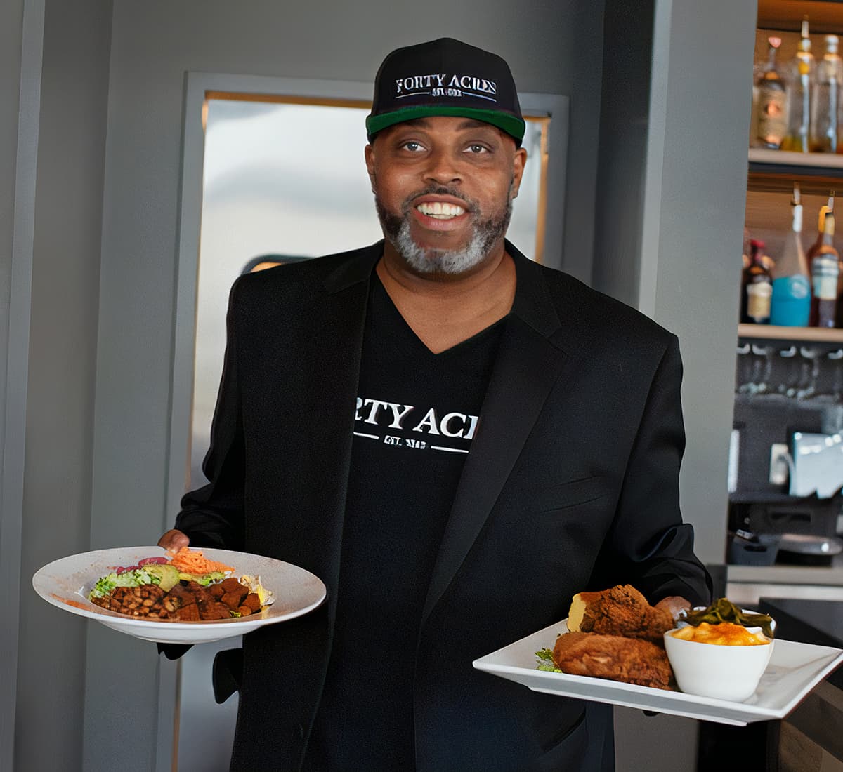 A man in a black suit carrying two plates of food in a restaurant
