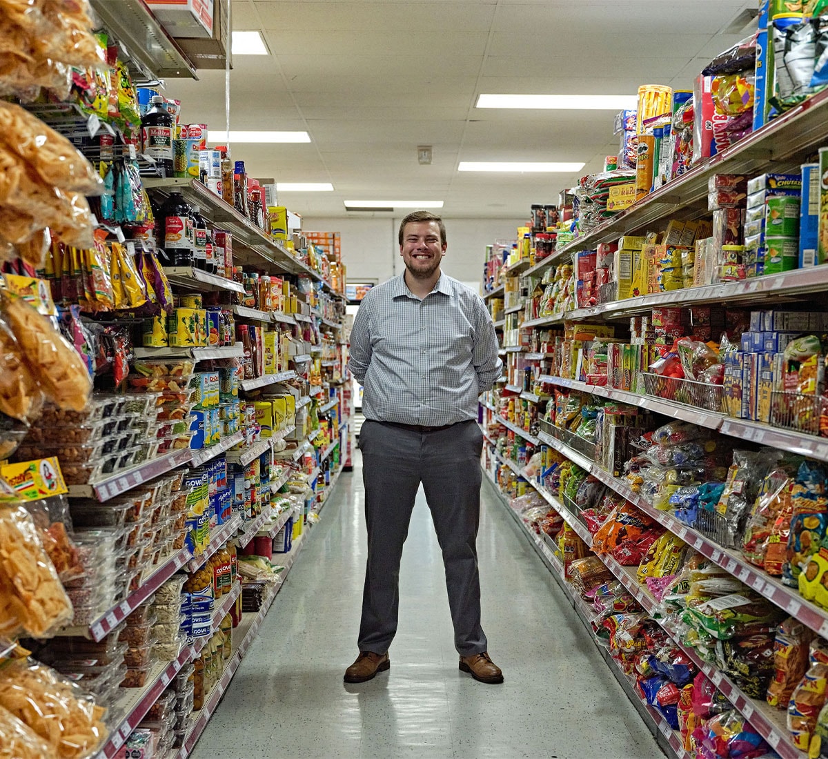 A man with a big smile is standing between shelves of food at a grocery store
