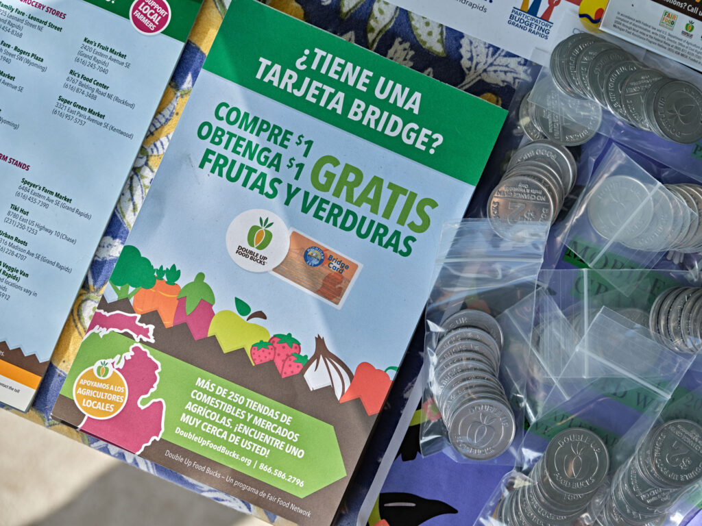 Flyer in Spanish about getting free fruits and vegetables, with bags of coins visible beside it.