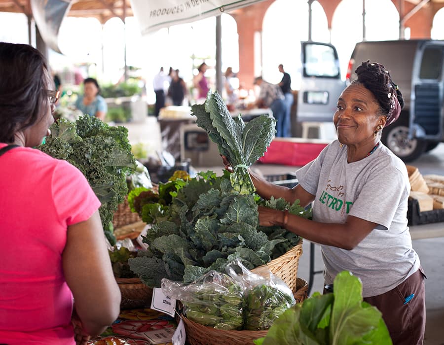 A woman bagging kale for a customer at the Detroit Farmers Market
