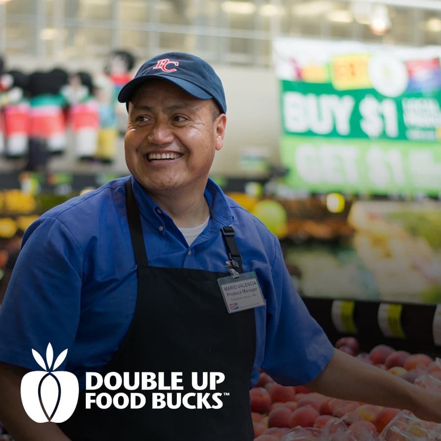 A grocery worker in a blue shirt and black apron is smiling while organizing peaches