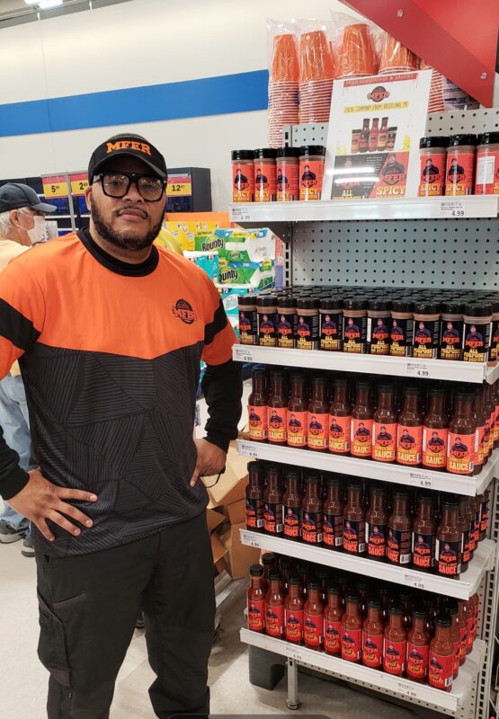 Antoine Williams of MFER Seasoning and Sauces standing next to his product on a stocked shelf.