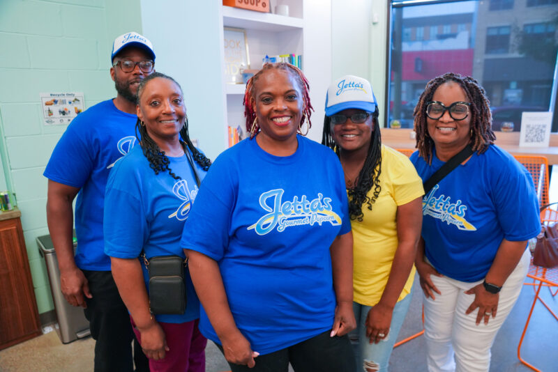 Five teammembers from Jetta's Gourmet Popcorn standing together wearing blue branded Jetta's t-shirts in a brightly lit indoor space.