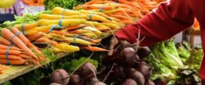 A person picking vegetables from a market stand with carrots and beets on display.