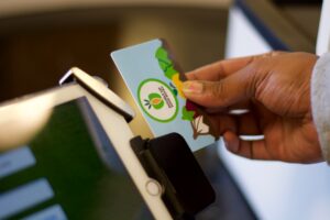 A hand holds a colorful card near a tablet in a card reader, ready for contactless payment.