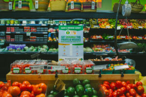 Fresh produce display with tomatoes, avocados, and a sign about doubling fruits and veggies with food benefits.