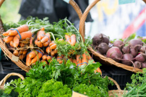 Baskets of fresh carrots, beets, and leafy greens displayed at a farmers market.