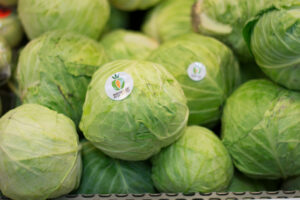 Several green cabbages with produce stickers are stacked together at a grocery store.