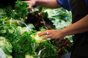 Person selecting fresh leafy lettuce at a grocery store display, surrounded by various greens.