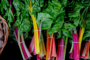 Bunches of rainbow chard with colorful stems and green leaves, tied with rubber bands, next to a basket.