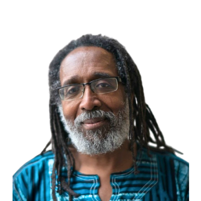 Older man with glasses, gray beard, and dreadlocks, wearing a blue patterned shirt, smiling slightly.