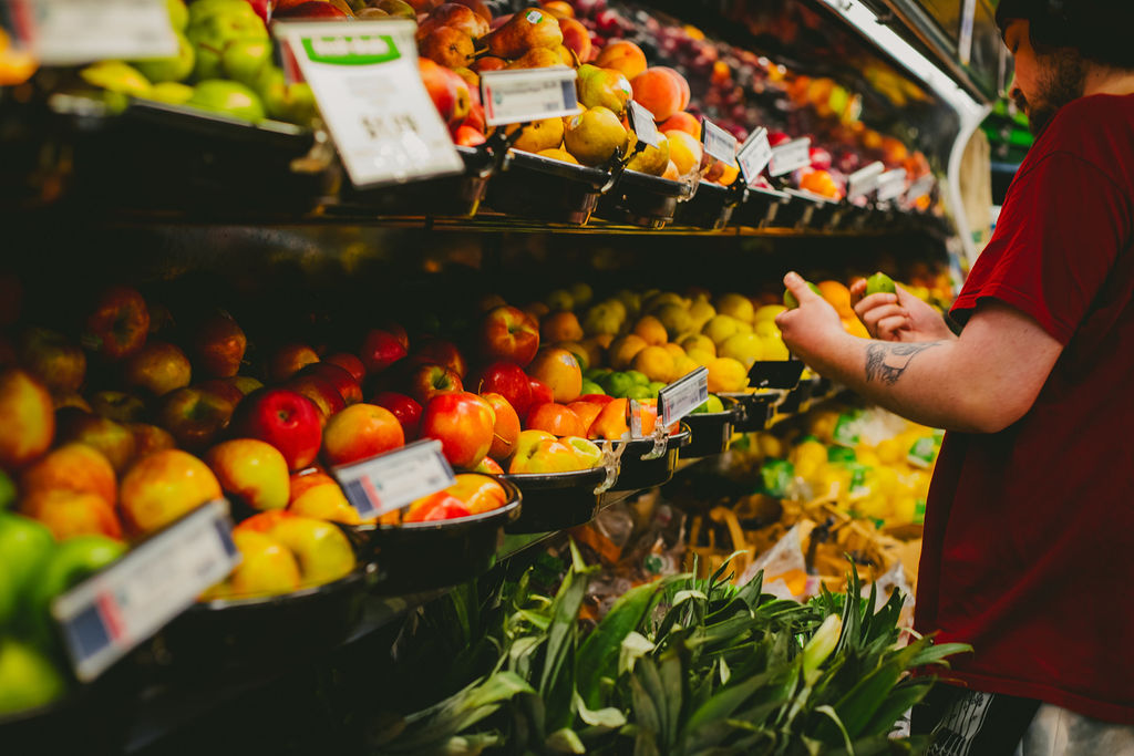 Person selects apples in a grocery store produce section filled with colorful fruits and vegetables.