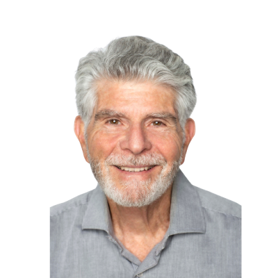 Smiling older man with gray hair and beard, wearing a light gray collared shirt, on a plain background.