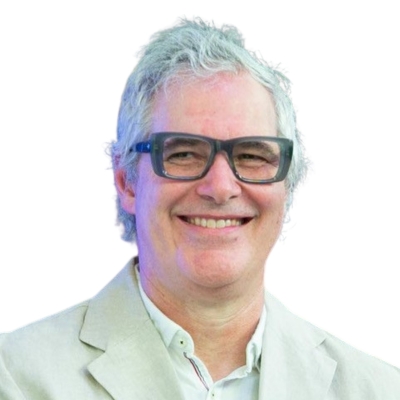 Smiling man with gray hair and glasses in a light suit jacket against a white background.