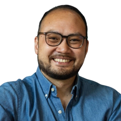 Smiling man with glasses and beard wearing a blue button-up shirt, on a white background.