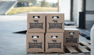 Four stacked Five Acre Farms boxes on a wooden pallet in an outdoor industrial area.