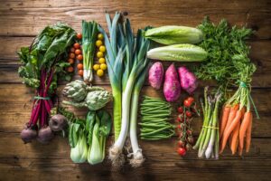 Assorted fresh vegetables, including carrots, lettuce, artichokes, and tomatoes, on a rustic wooden table.