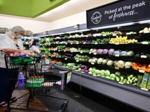 Two women shop for fresh produce at a grocery store, both wearing masks and pushing shopping carts.