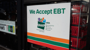 Sign on a store window reads We Accept EBT - SNAP Supplemental Nutrition Assistance Program..