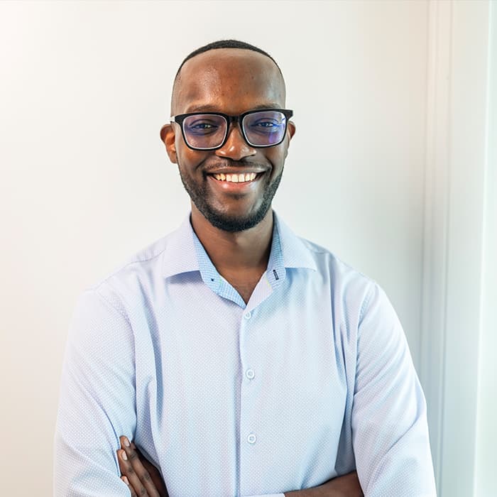 Smiling man in glasses and a light blue shirt stands with arms crossed against a white background.