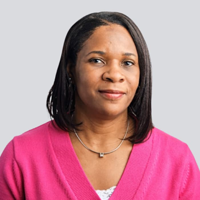 Woman with straight dark hair wearing a pink sweater and silver necklace, smiling slightly at the camera.