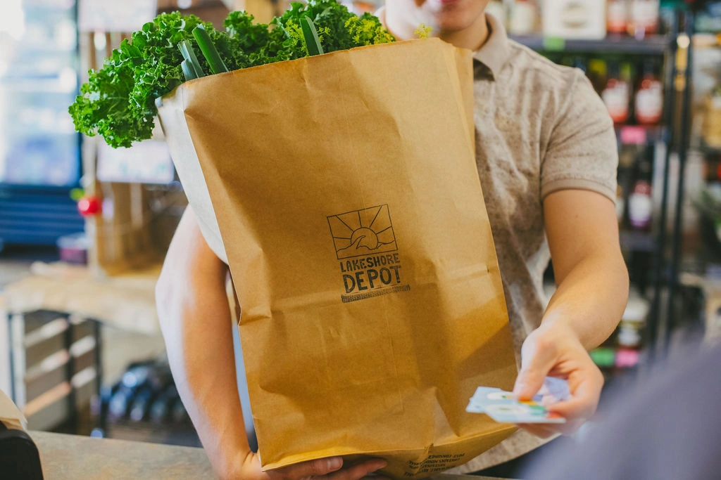 Person holding a paper bag with green vegetables, handing a card at a store counter.