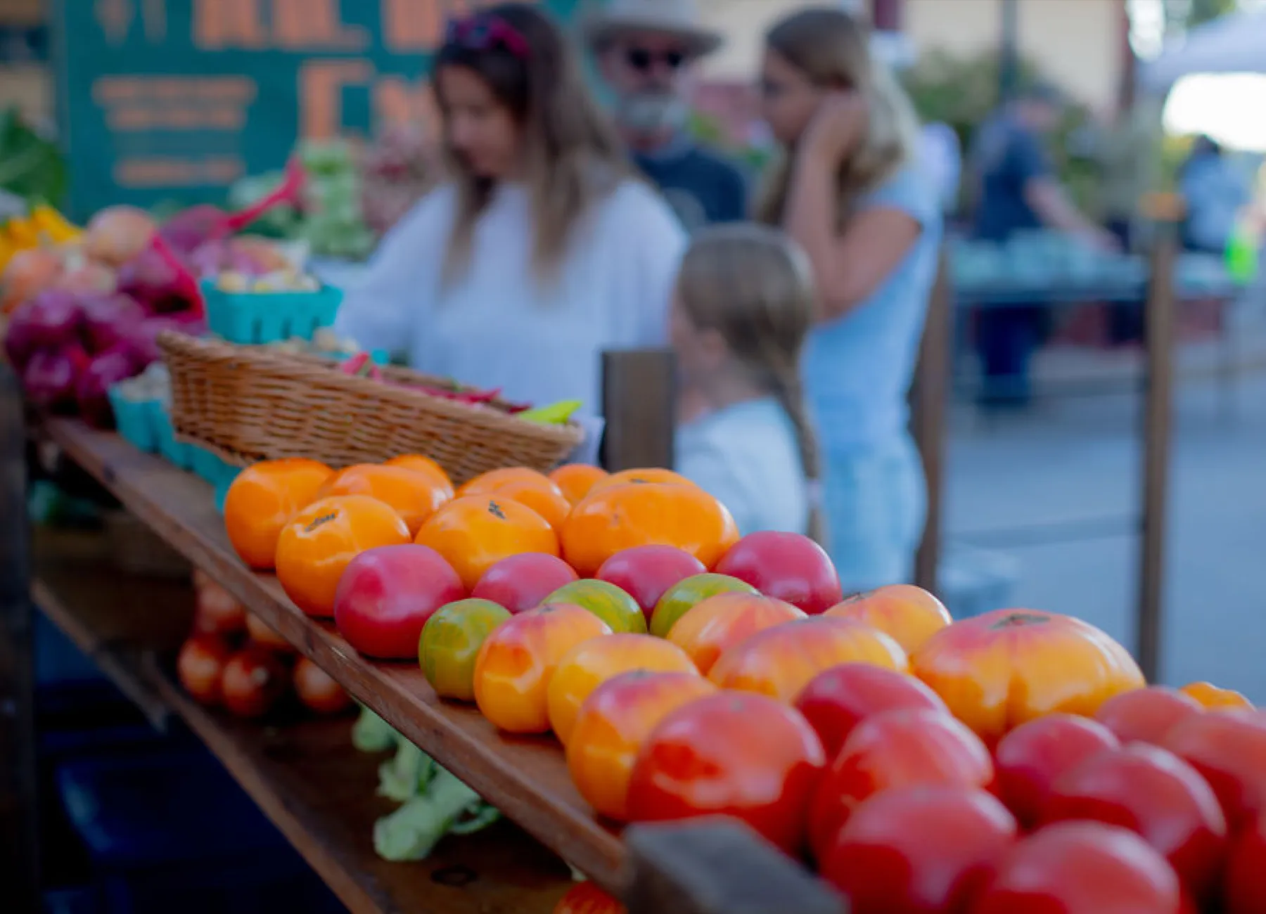 Heirloom tomatoes on display at an outdoor market with people browsing in the background.